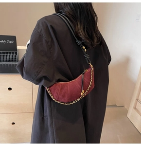 Detailed view of burgundy suede crescent bag with metal chain on model shoulder