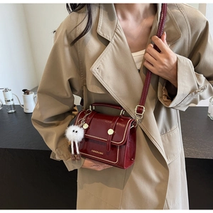 Detail view of burgundy patent leather bag with gold buckle and plush charm on trench coat