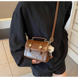 Detail of a brown leather crossbody bag with gold hardware and white plush charm