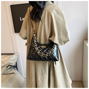 Detail of black quilted patent leather bag with gold chain strap on beige trench coat