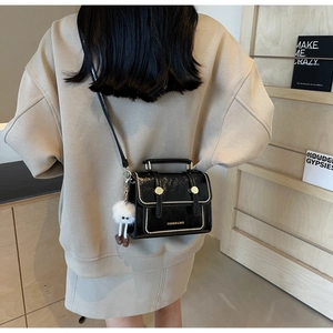 Detail view of black patent leather crossbody bag with white beads and plush charm