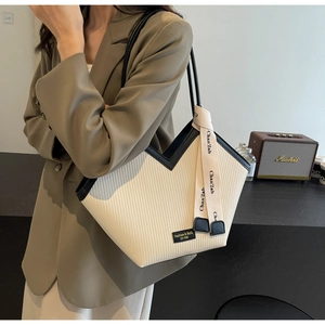 Detail of cream tote bag featuring vertical pleated texture and black leather piping