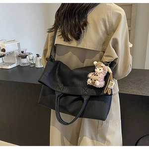 Detail of black large tote bag with lychee texture being worn by a model in a cafe