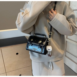 Detail of black glossy shoulder bag with gold rivets and cute plush doll pendant