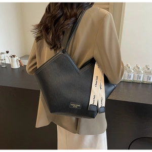 Detail of black tote bag featuring vertical embossed texture and decorative strap