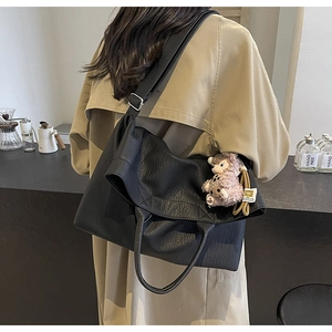 Detail of black textured leather tote bag with wide strap and plush bear charm