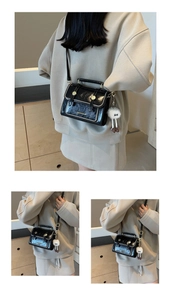 Detail of glossy black patent leather bag with gold rivets and plush charm accessory