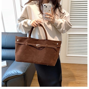 Detailed macro view of dark brown suede tote bag with decorative buckle and metal rivets