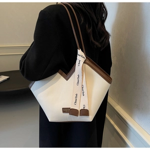 Detail of white pleated tote bag with brown leather accents and a stylish lettered strap