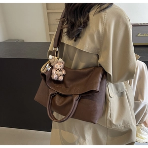 Detail view of large dark brown leather tote bag with a small plush bear charm attached
