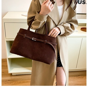 Detail of dark brown faux suede tote bag with decorative metal buckle on a model