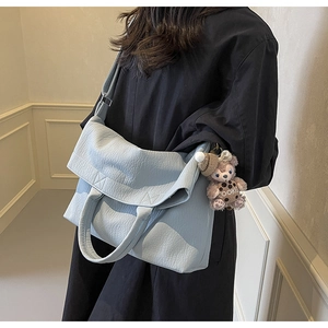 Detail of light blue pebble leather tote bag with soft texture and plush cookie charm