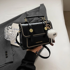 Retro black crossbody bag with gold rivets and white plush charm on a grey background