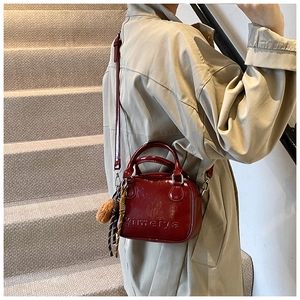 Detail of dark red patent leather handbag with pom-pom charm and woven rope decoration