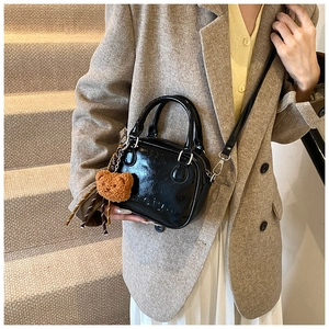 Detail of black patent leather bowling bag with plush bear charm and crossbody strap