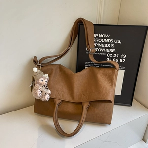 Caramel brown leather tote bag with long strap and cute plush charm in minimalist studio