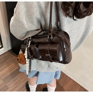 Detail of dark brown glossy underarm bag featuring silver buckles and cute plush bear charm