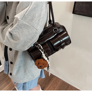 Close-up of a glossy dark brown shoulder bag featuring front pockets and a cute puppy charm