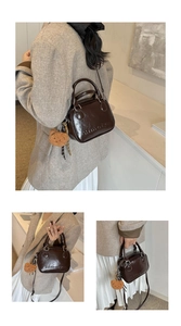 Detail of dark brown glossy Boston bag featuring a plush bear charm and embossed logo