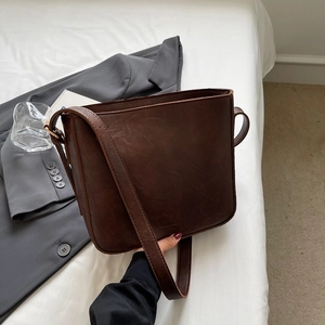 Sac cabas vintage en cuir marron foncé avec large bandoulière sur fond de literie blanche