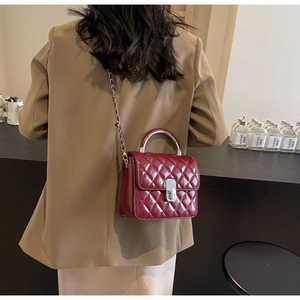 Détail du sac bandoulière matelassé bordeaux avec chaîne argentée sur un mannequin