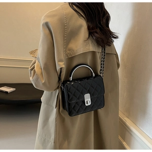 Sac bandoulière matelassé noir avec chaîne argentée porté sur un trench beige