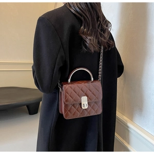 Détail d'un sac bandoulière marron matelassé avec poignée en métal argenté et chaîne