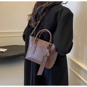 Sac seau marron rétro texturé avec poignées porté par un mannequin en manteau noir