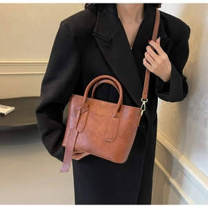 Détail du sac seau marron caramel avec doubles poignées et boucles dorées sur blazer