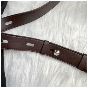 Detail of dark brown leather strap with silver stud and adjustable holes on plush background
