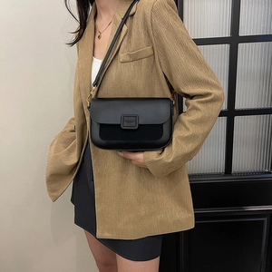 Fashionable black leather square shoulder bag with gold hardware worn by a model in a blazer