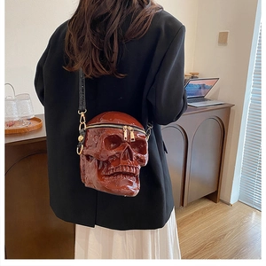 Detail of dark brown skull crossbody bag featuring glossy finish and gold zipper closure
