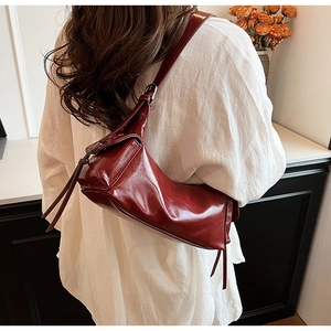 Detail of burgundy patent leather shoulder bag with tassels and silver metal buckles