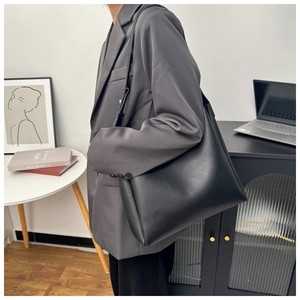 Minimalist black leather tote bag with long strap worn on shoulder in modern interior