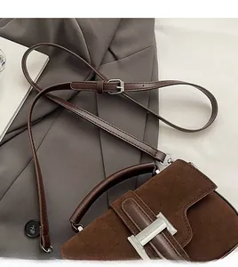Détail d'un sac bandoulière en daim marron foncé avec boucle argentée sur tissu