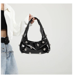 Detail of glossy black leather tote bag featuring large silver spherical metal rivets