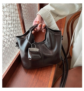 Dettaglio di borsa vintage in pelle marrone scuro con ciondolo mini borsa su davanzale in legno