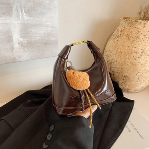 Brown polished leather saddle bag with gold metal buckle and orange pompom accessory