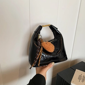 Glossy black hobo shoulder bag with gold buckle and plush ball charm in hand