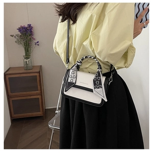 Detail of cream crossbody bag with black trim and silk scarf handle decoration