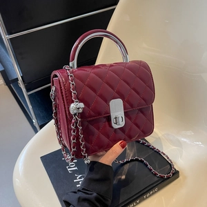Sac matelassé bordeaux avec bandoulière chaîne argentée et poignée sur chaise crème