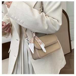 Detail of beige square crossbody bag with patterned silk ribbon on strap and leather texture