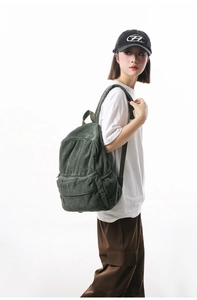 Detailed texture of dark green corduroy backpack showing vertical ribbed fabric and front pocket