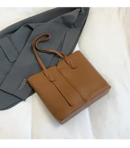 Gros plan sur un sac cabas en cuir marron avec lanières à rivets sur fond de veste