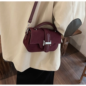 Détail du sac bandoulière bordeaux en daim avec boucle argentée sur un manteau beige