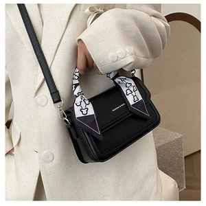 Detail of black pebbled leather crossbody bag with decorative heart ribbon handle