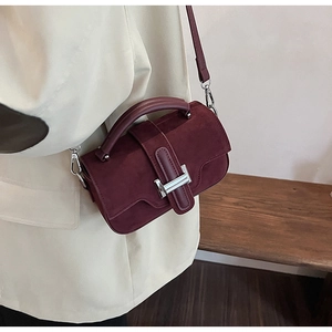 Détail d'un sac en daim bordeaux avec fermoir argenté en H sur un blazer beige