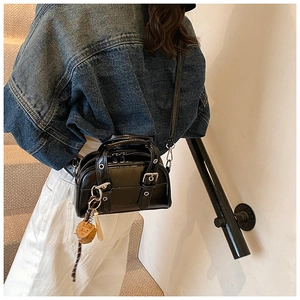 Détail du sac à bandoulière en cuir noir brillant avec boucles et pendentif baseball