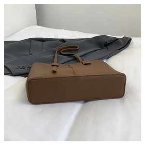 Détail du sac fourre-tout en cuir grainé marron caramel posé sur un tissu blanc doux