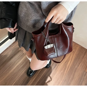 Dettaglio della borsa in pelle cerata bordeaux con finitura lucida e mini charm